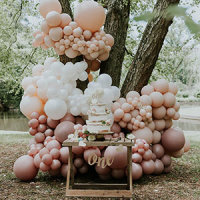 a pink and white balloon garland set up on a tree in a forest