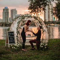 A man proposing to his girlfriend by the beach next to a luxurious picnic set up with an igloo tent